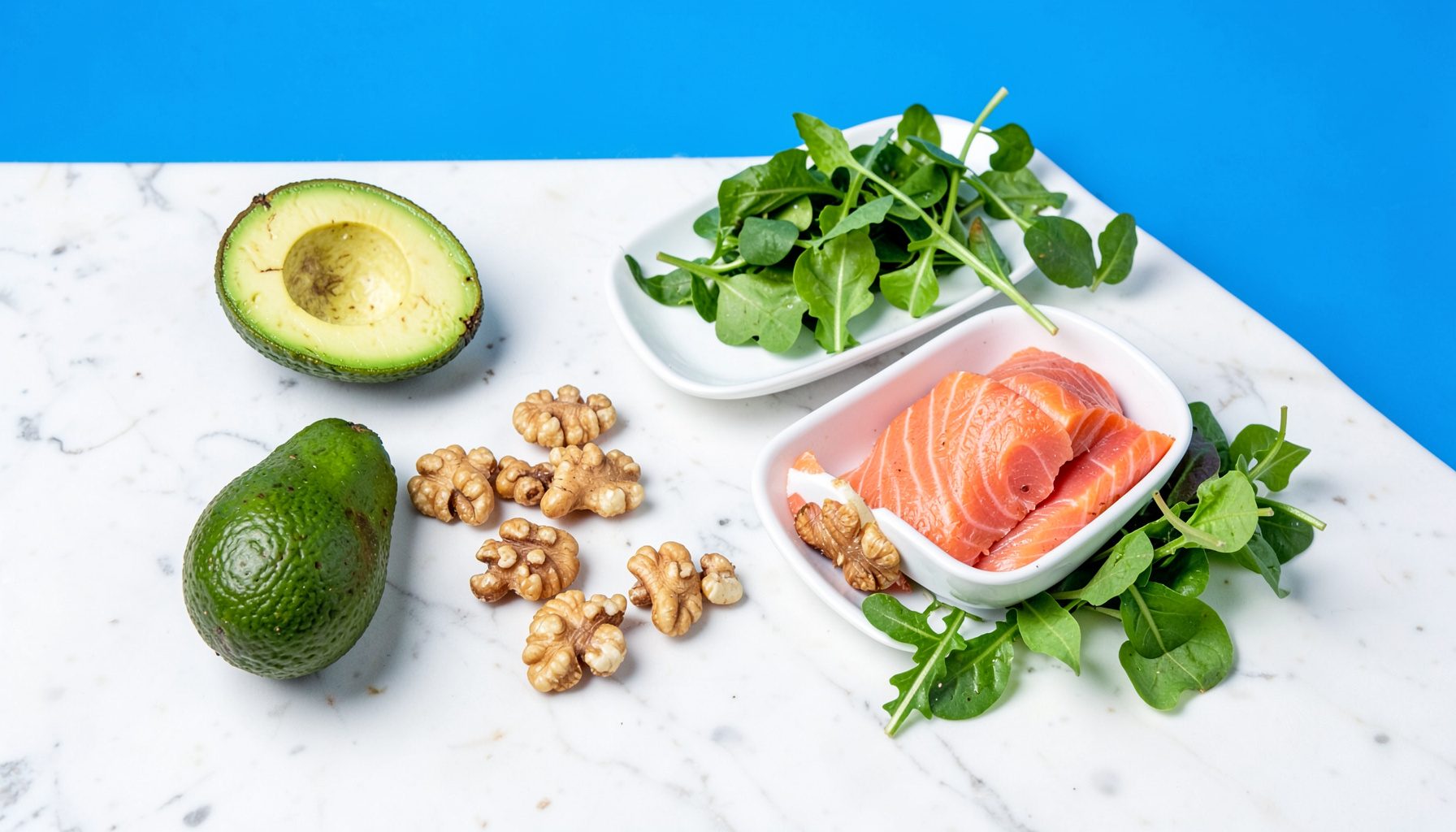 A flat lay of keto-friendly foods on a light marble surface: avocado, nuts, salmon, and fresh greens in soft natural daylight.