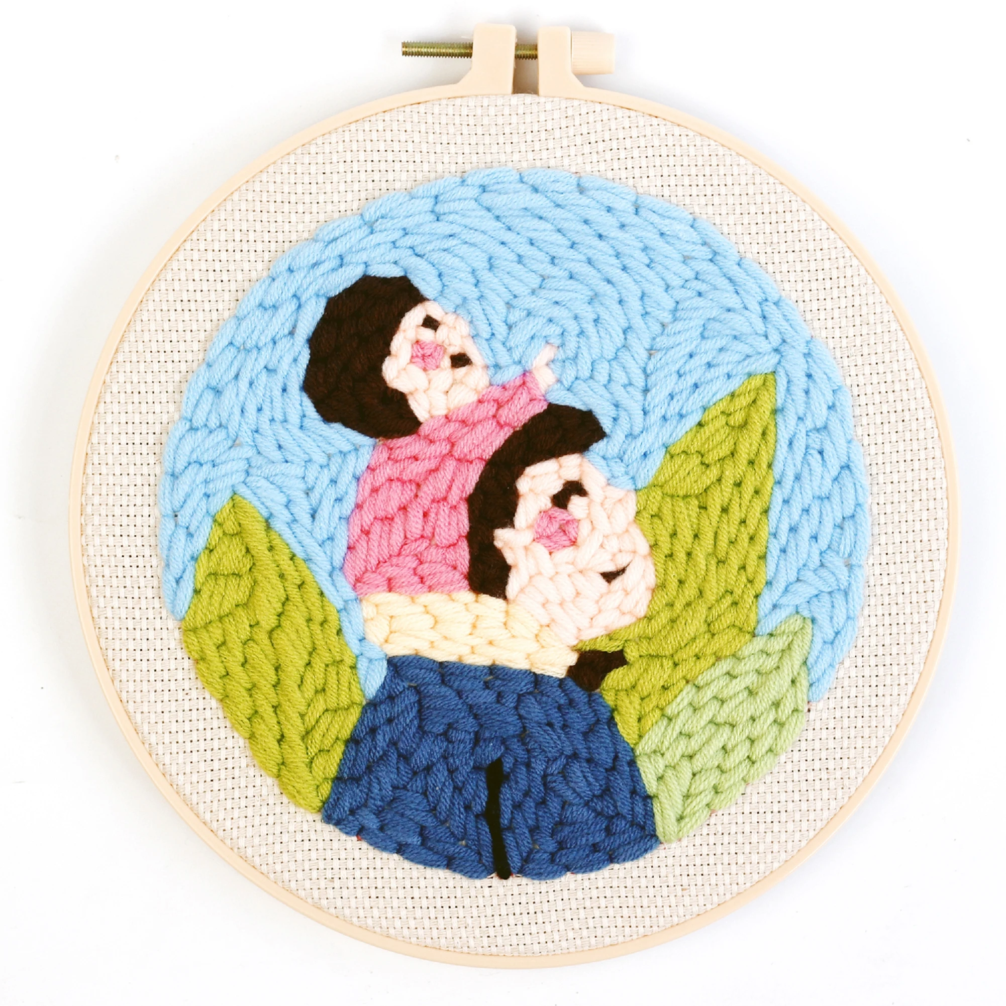 A round embroidery hoop artwork depicting two stylized figures with dark hair against a blue background with green leaf motifs